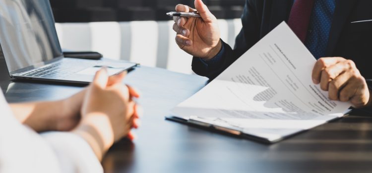 Businessman in suit in his office showing an insurance policy and pointing with a pen where the policyholder must to sign. Insurance agent presentation and consulting insurance detail to customer.